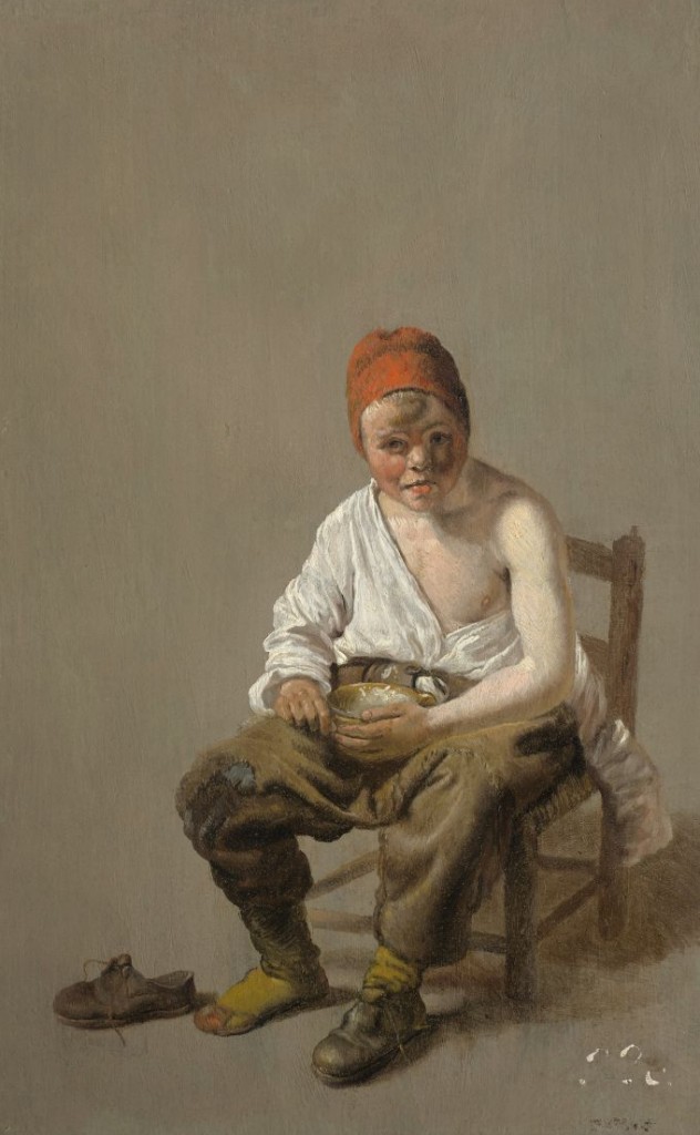 Portrait of a seated young boy wearing a white shirt that is half off his body, a red hat, and one shoe. He eats a bowl of porridge.