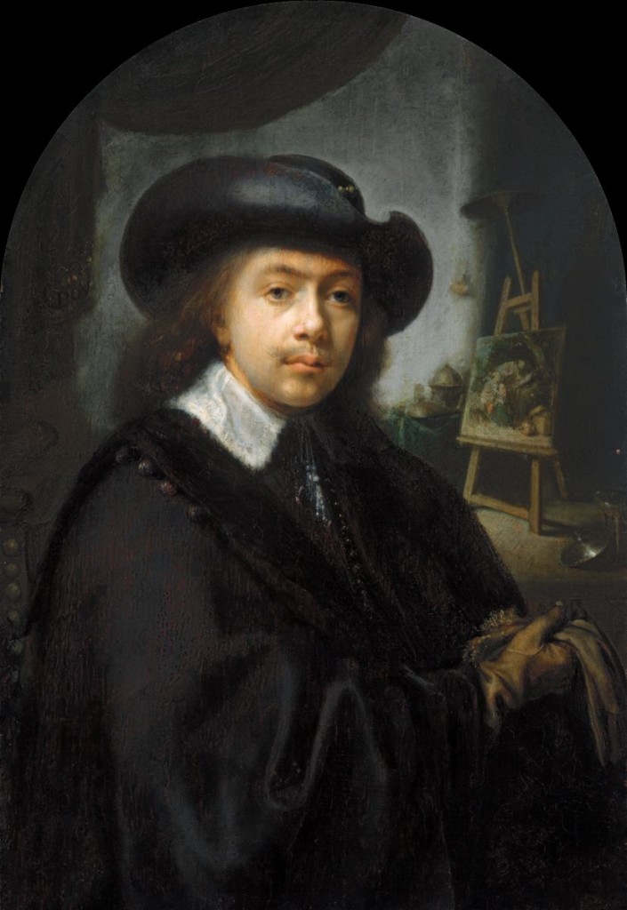 Self-portrait of a male artist wearing all black and a black hat, sitting in his studio.