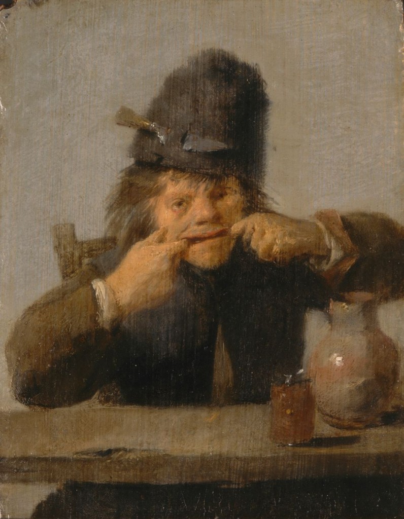 A young boy making a silly face. He wears a tall hat and sits behind a table.